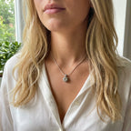 Close-up of a person wearing the white topaz alto pendant, blurred background