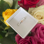 Silver and gold ring in a box surrounded by colourful roses with a blurred background