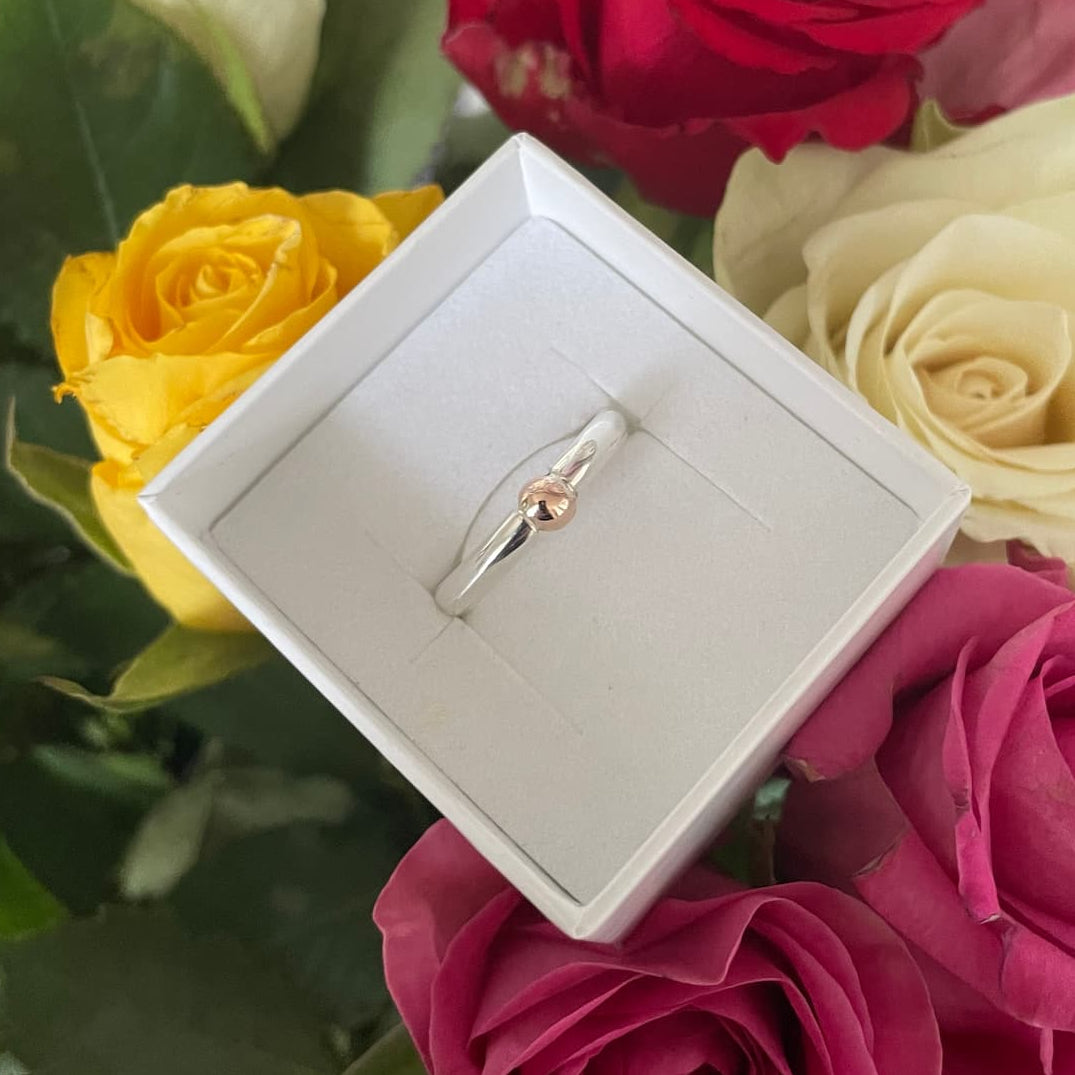 Silver and gold ring in a box surrounded by colourful roses with a blurred background