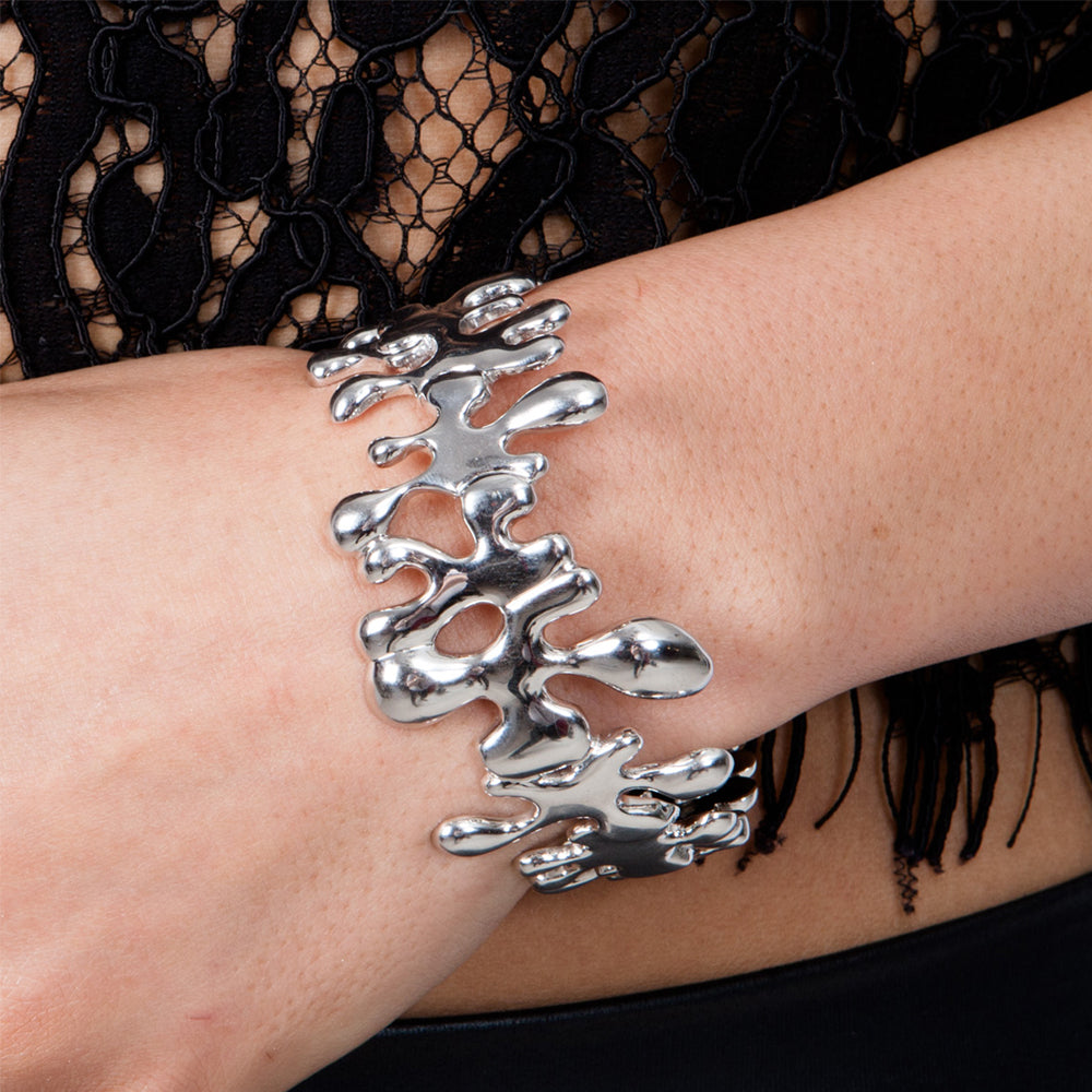 Silver splat cuff on a wrist with a black lace garment in the background
