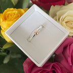 Silver and gold ring in a box surrounded by colourful roses with a blurred background