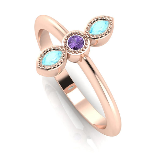 Angled perspective of an 18ct rose gold trilogy ring with violet sapphire and marquise aquamarines featuring fine milgrain textured edges.